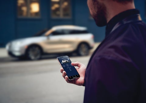 A person is shown interacting with a smartphone to connect to a Lincoln vehicle across the street. | Joe Cooper Lincoln of Edmond in Oklahoma City OK